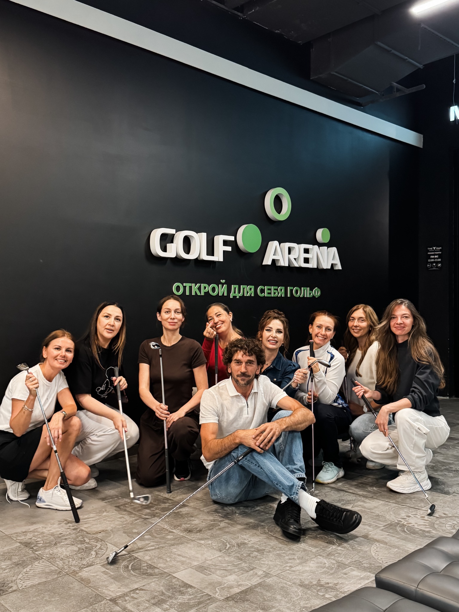 Компания гостей с клюшками на фоне логотипа Golf Arena